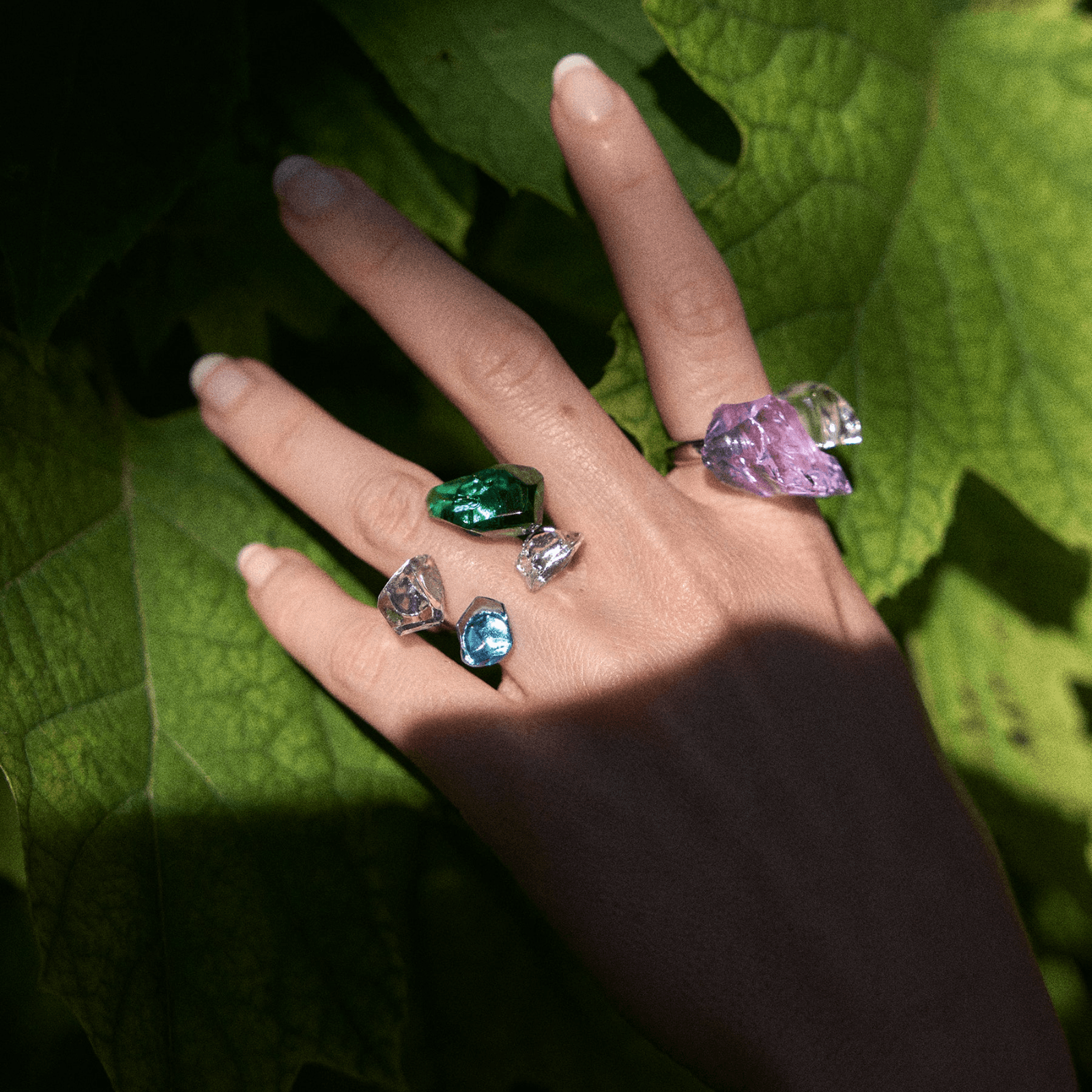 Hand wearing colored glass cocktail rings against a large green leaf