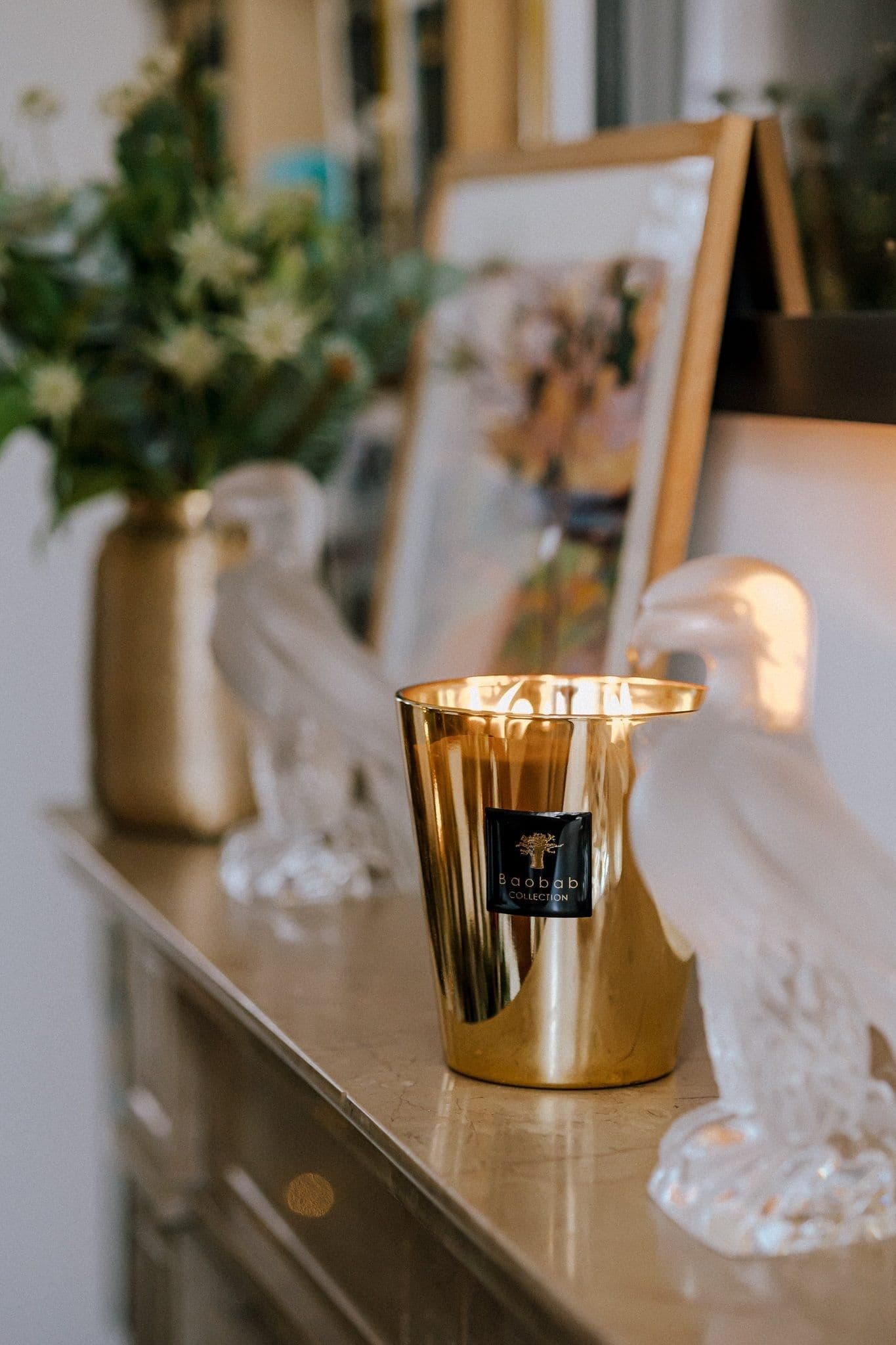 Baobab Aurum gold candle on a console beside glass bird figures and flowers