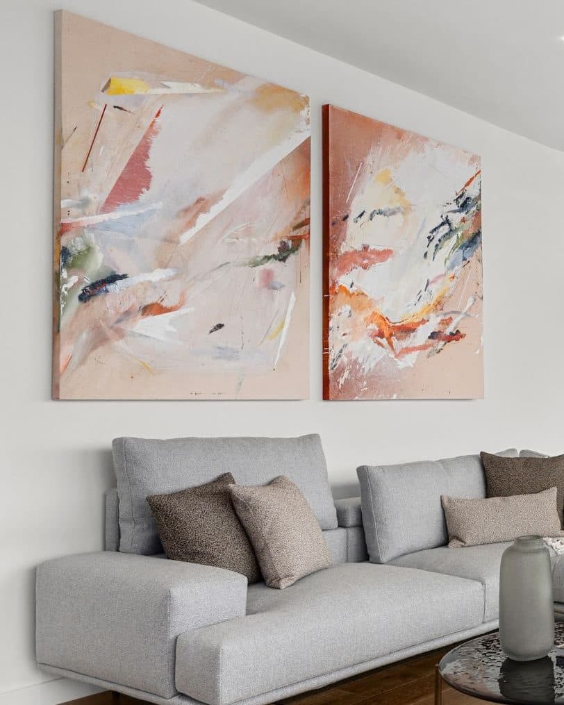 Two large abstract paintings in blush, terracotta and white above a light grey sectional sofa