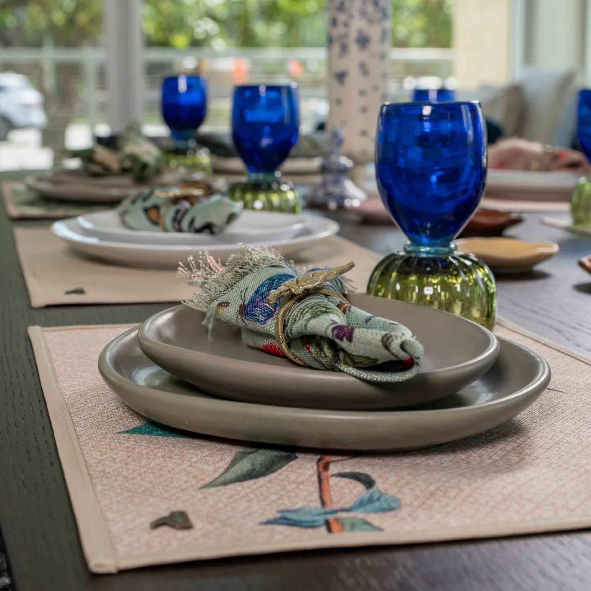 Table set with cobalt Duo Glass goblets, grey stoneware plates and printed napkins on patterned placemats