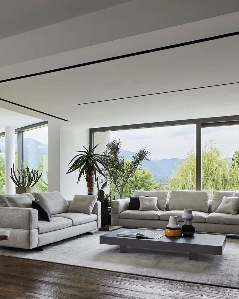 Living room with two light grey fabric sofas, a low charcoal coffee table and floor-to-ceiling windows onto a mountain view