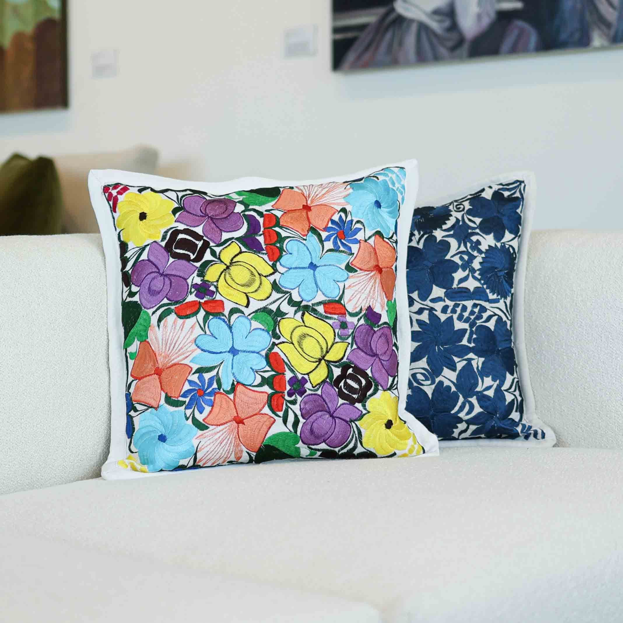 Embroidered Oaxacan floral pillow in bright colors beside a navy floral pillow on a white sofa