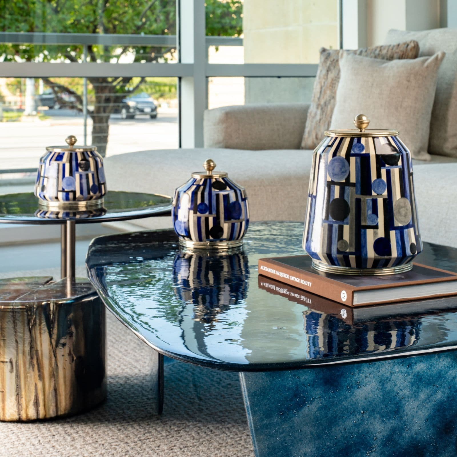 Blue and ivory patterned Lunares ceramic vases with metal lids on a blue glass coffee table