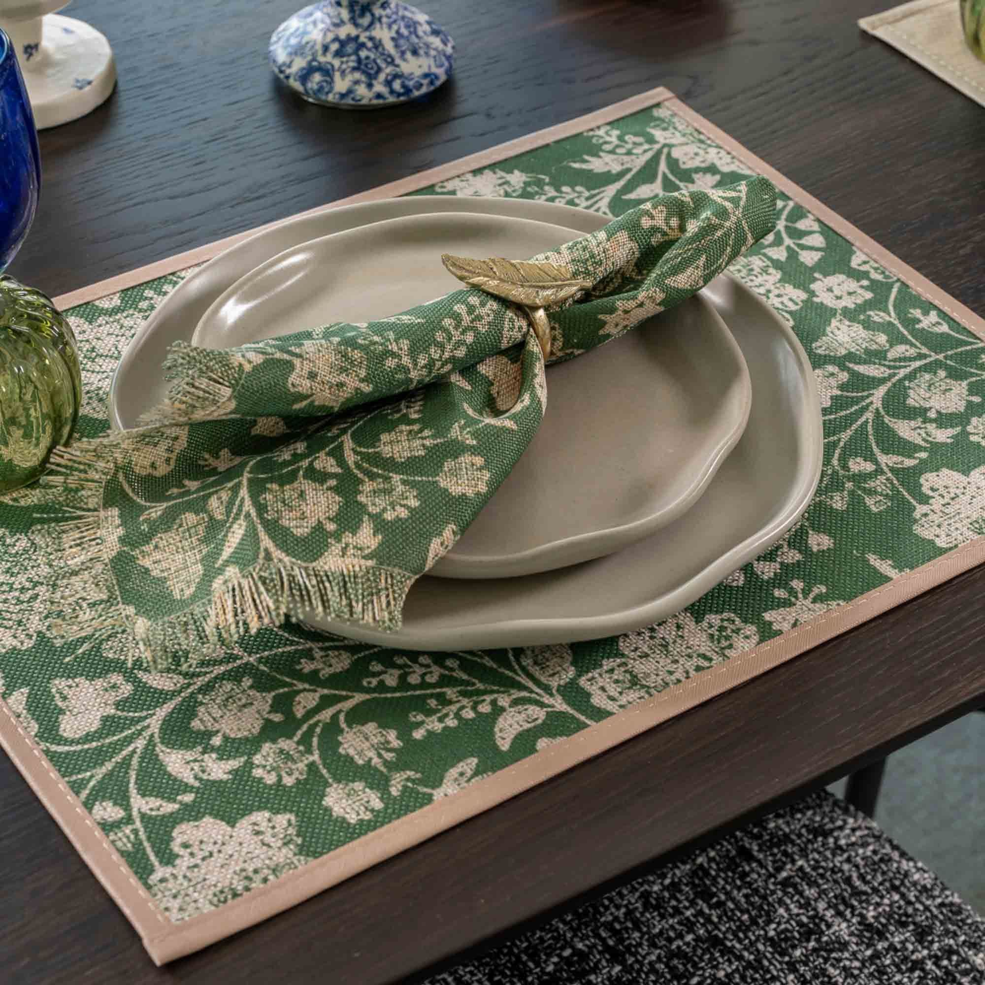 Green floral napkin with a gold napkin ring on grey plates over a green floral placemat